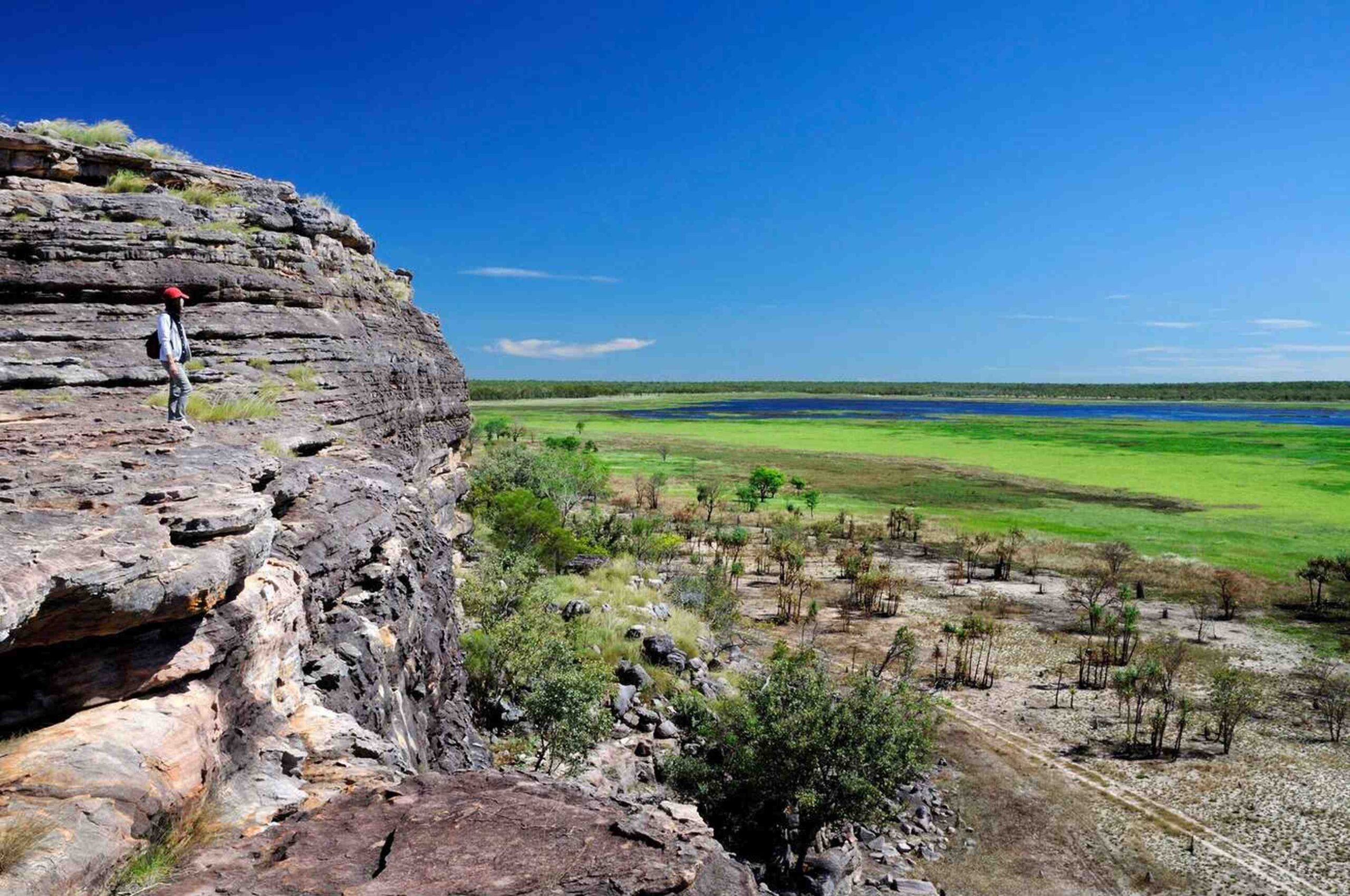 A breathtaking view of Kakadu National Park, showcasing dramatic cliffs, lush greenery, and wetlands under a vibrant blue sky.