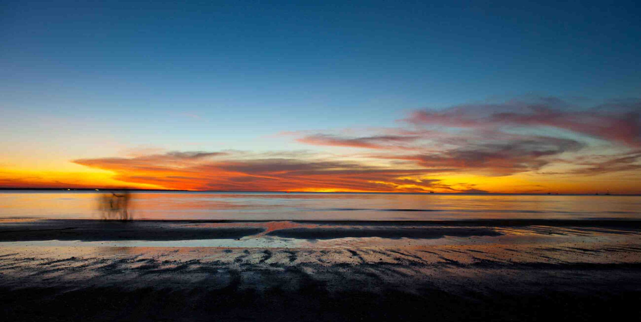 A stunning sunset over Mindil Beach in Darwin, showcasing vibrant orange and blue hues reflecting on the calm waters