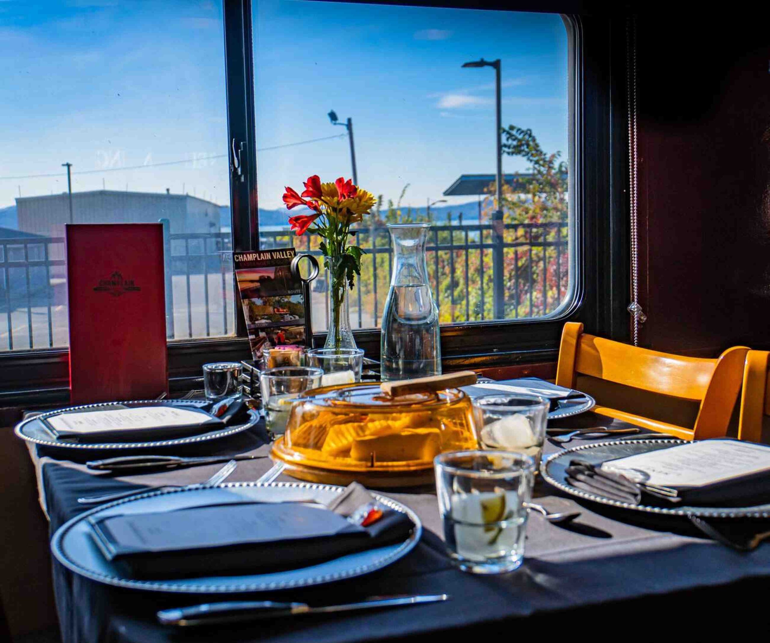 A beautifully set dining table aboard a train, featuring elegant dishes, fresh flowers, and scenic views through the window.