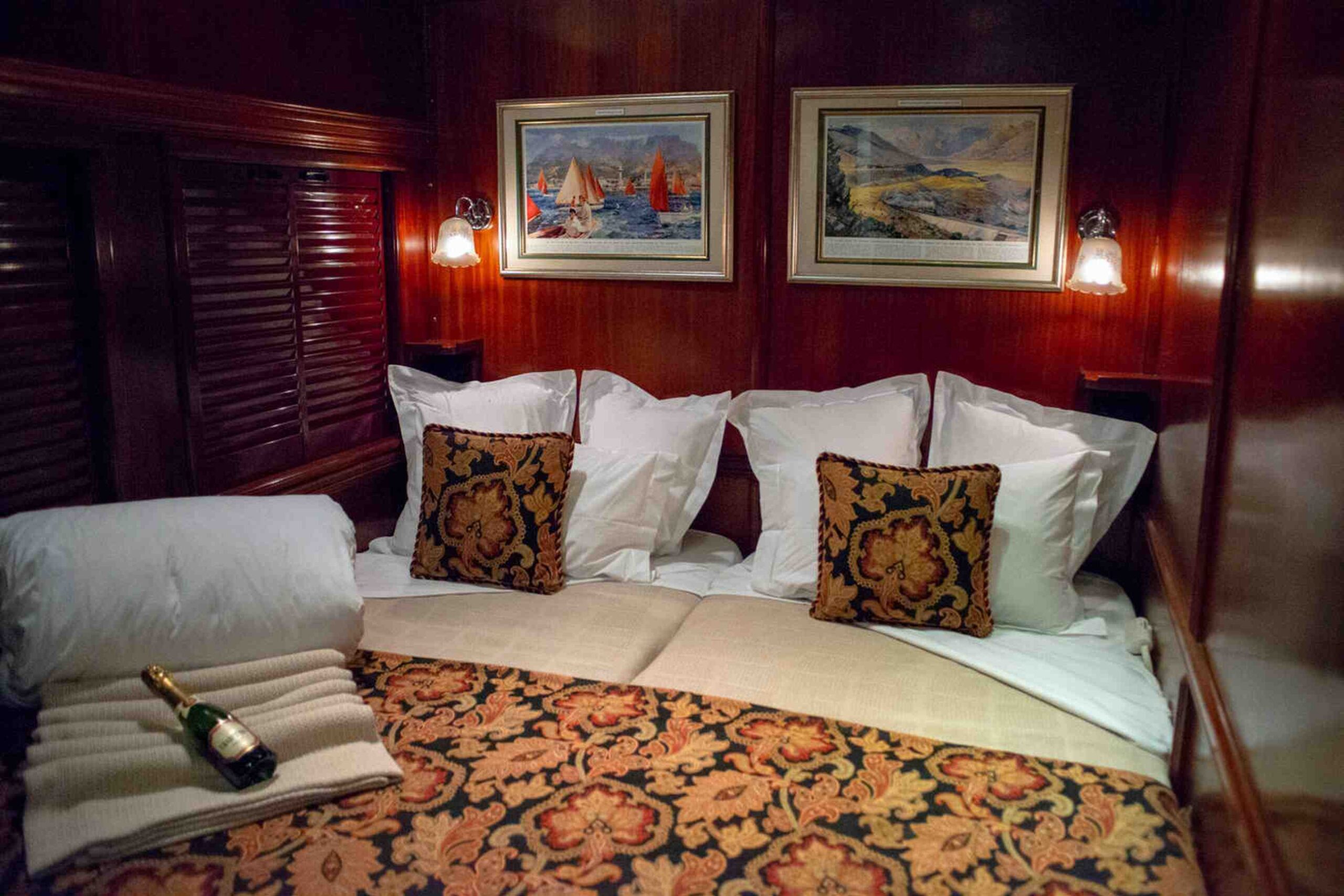 Luxurious interior of a Ghan train cabin featuring plush bedding, decorative pillows, and a warm wooden finish for a cozy ambiance.