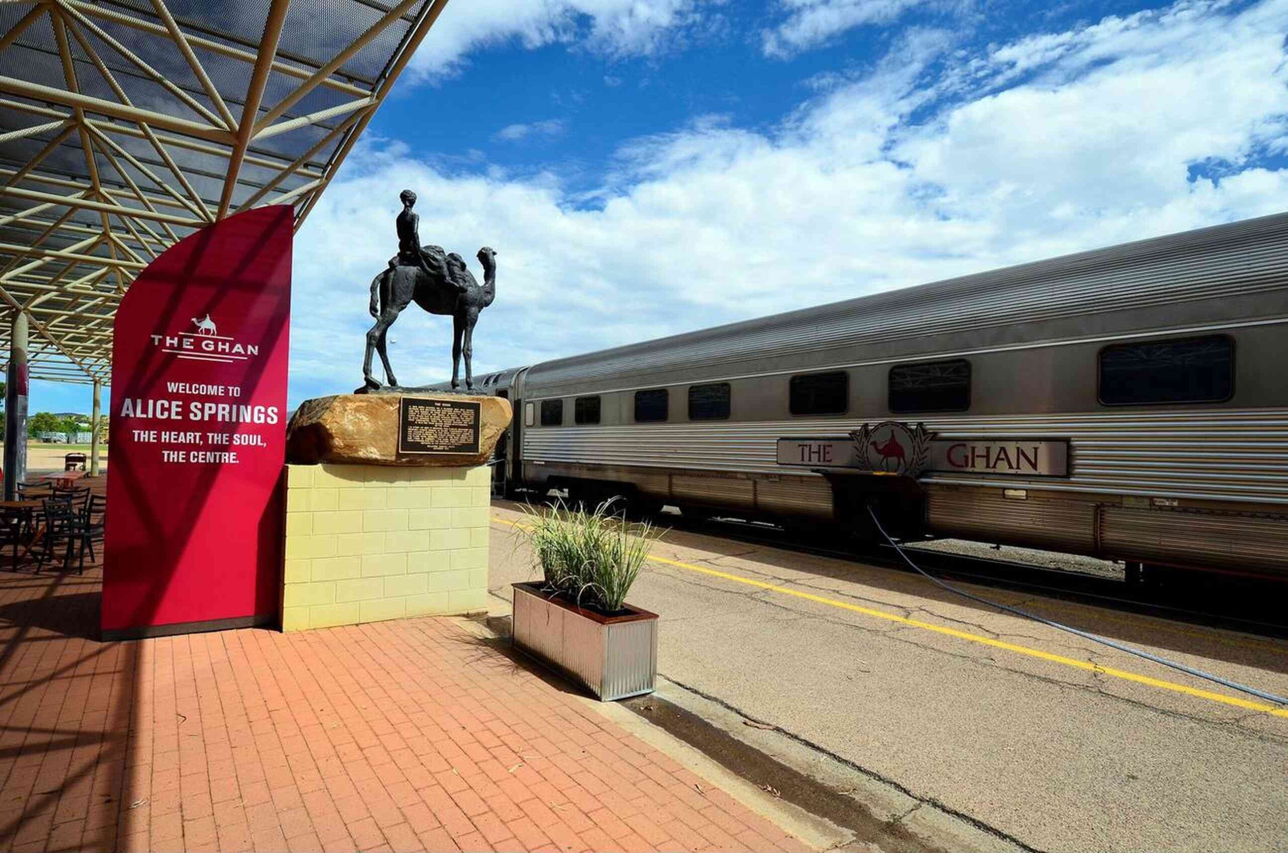 View of The Ghan train at Alice Springs station with the iconic camel statue nearby.